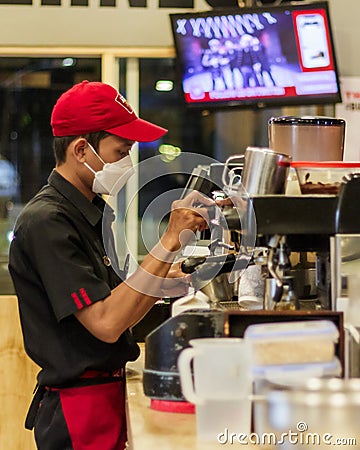 Handsome barista waring a red hat and white masker making a cup of coffee Editorial Stock Photo