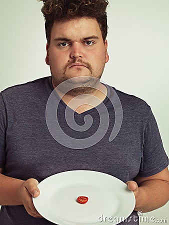 You have got to be kidding me. Portrait of an overweight man holding a plate with a tiny sliver of tomato. Stock Photo