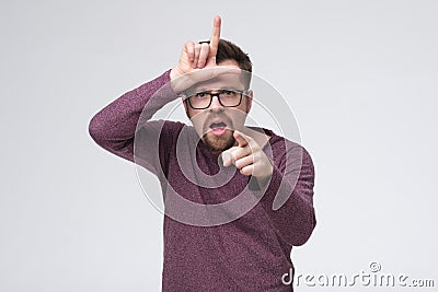 You are loser. Young man with loser sign on forehead pointing on you. Stock Photo