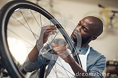 You see a bike, I see greener grass. a young man fixing a wheel at a bicycle repair shop. Stock Photo