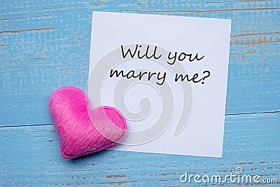 YOU WILL MARRY ME? word on paper note with pink heart shape decoration on blue wooden table background. Love, Wedding, Romantic Stock Photo