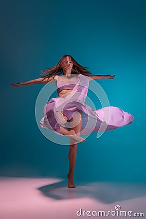 Young adorable flexible contemp dancer in lilac dress dancing on gradient blue white background in neon. Stock Photo