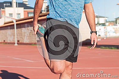 Young adult athlete man doing warm-up exercises and stretching the muscles of his legs, quadriceps and calves to avoid serious Stock Photo