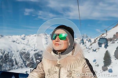 Young adult beautiful happy attractive caucasian smiling woman enjoy ascent sitting inside ski lift gondola cable car against Stock Photo