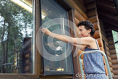 Young adult beautiful slim sporty caucasian woman stand on metal ladder and installing window mosquito insect fly screen Stock Photo