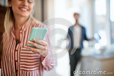 Young adult blonde holding her cell phone, in focus, with blurry person in the beackground Stock Photo