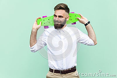 Young adult businessman, holding under head his skate,looking left and toothy smiling. Light green background. Stock Photo