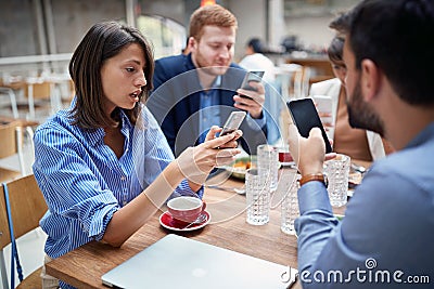 Young adult businesspeople at lunch in a restaurant checking their cell phones for any good news after coronavirus. covid 19, Stock Photo