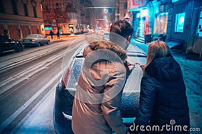 Young adult couple draws a heart on snow covered car Stock Photo