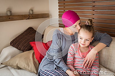 Young adult female cancer patient spending time with her daughter at home, relaxing on the couch. Cancer and family support. Stock Photo