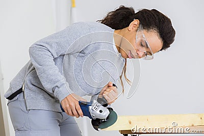 Young adult female worker grinding plank with electric grinder Stock Photo