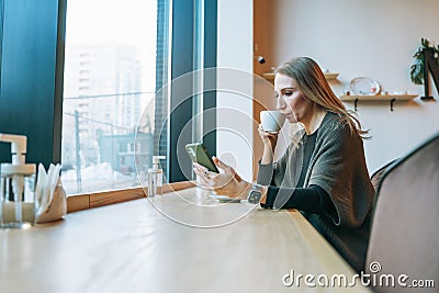 Young adult forty years blonde woman in casual clothes drinking coffee using mobile at cafe Stock Photo