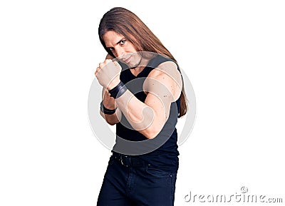 Young adult man with long hair wearing goth style with black clothes ready to fight with fist defense gesture, angry and upset Stock Photo