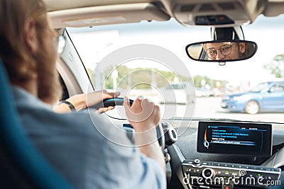 Young adult man sitting in car, looking at rear view mirror Stock Photo