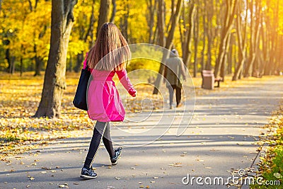 Young adult woman in bright casual coat walking along beautiful golden colored autumn park alley. Happy attractive sporty girl in Stock Photo