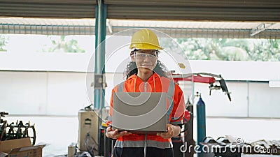 Young Africa American engineer wearing safety helmet and glasses holding the laptop and walking and smile in the robotic arm Stock Photo
