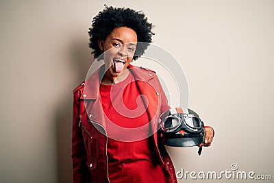 Young African American afro motorcyclist woman with curly hair holding motorcycle helmet sticking tongue out happy with funny Stock Photo
