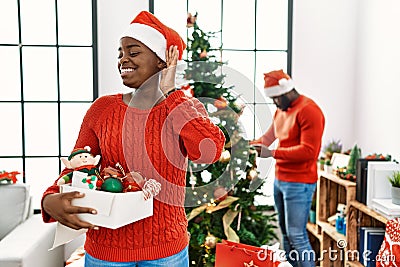 Young african american couple standing by christmas tree smiling with hand over ear listening an hearing to rumor or gossip Stock Photo