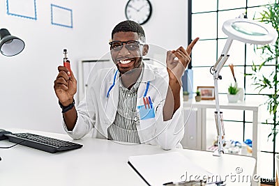 Young african american doctor man holding electronic cigarette at medical clinic smiling happy pointing with hand and finger to Stock Photo