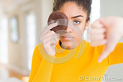 Young african american girl eating sweet chocolate donut with angry face, negative sign showing dislike with thumbs down, Stock Photo