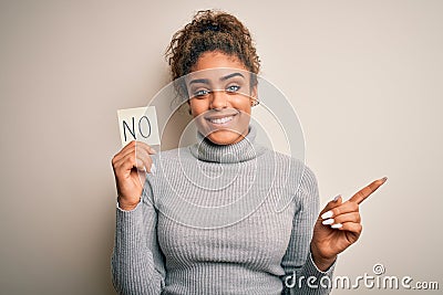 Young african american girl holding reminder paper with no word negative message very happy pointing with hand and finger to the Stock Photo