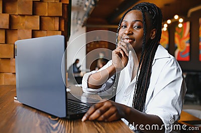 Young African American girl sitting in restaurant and typing on her laptop. Pretty girl working on computer at cafe Stock Photo