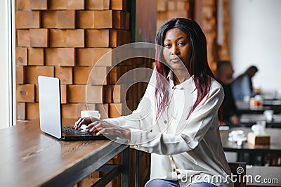 Young African American girl sitting in restaurant and typing on her laptop. Pretty girl working on computer at cafe Stock Photo