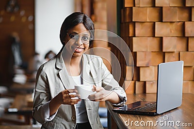 Young African American girl sitting in restaurant and typing on her laptop. Pretty girl working on computer at cafe Stock Photo