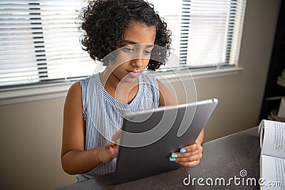 Young African American girl student studying using a computer tablet and textbook Stock Photo