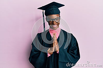 Young african american girl wearing graduation cap and ceremony robe praying with hands together asking for forgiveness smiling Stock Photo