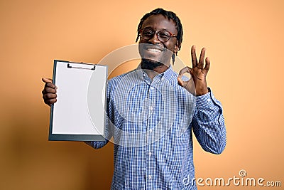 Young african american inspector man wearing glasses holding clipboard checklist doing ok sign with fingers, excellent symbol Stock Photo