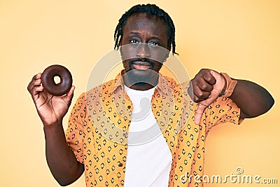 Young african american man with braids holding donut with angry face, negative sign showing dislike with thumbs down, rejection Stock Photo