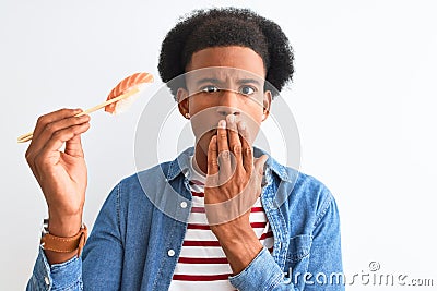 Young african american man eating nigiri using chopsticks over isolated white background cover mouth with hand shocked with shame Stock Photo