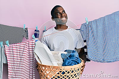 Young african american man holding laundry basket smiling looking to the side and staring away thinking Stock Photo