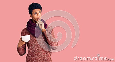 Young african american man wearing winter scarf and drinking a cup of hot coffee serious face thinking about question with hand on Stock Photo