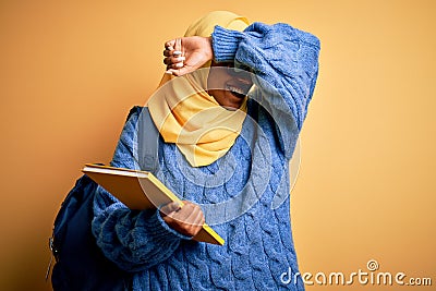 Young African American student woman wearing muslim hijab and backpack holding book Smiling cheerful playing peek a boo with hands Stock Photo