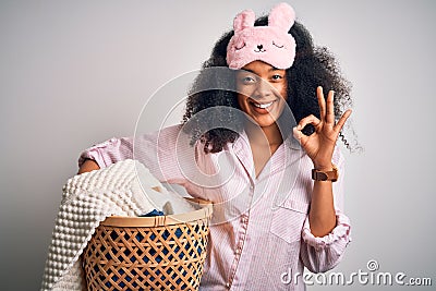 Young african american woman with afro hair wearing pajama doing laundry domestic chores doing ok sign with fingers, excellent Stock Photo