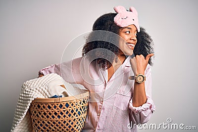 Young african american woman with afro hair wearing pajama doing laundry domestic chores pointing and showing with thumb up to the Stock Photo