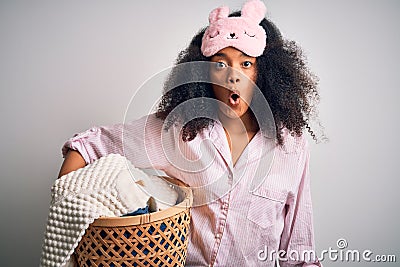 Young african american woman with afro hair wearing pajama doing laundry domestic chores scared in shock with a surprise face, Stock Photo