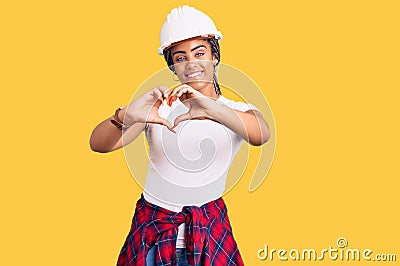 Young african american woman with braids wearing hardhat and builder clothes smiling in love showing heart symbol and shape with Stock Photo