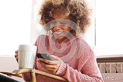 Young african american woman drinking hot cup of coffee and looking at cellphone Stock Photo