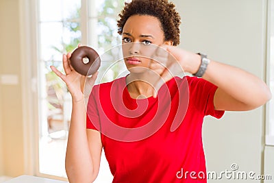 Young african american woman eating chocolate donut with angry face, negative sign showing dislike with thumbs down, rejection Stock Photo