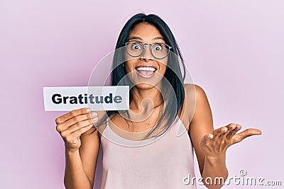 Young african american woman holding gratitude message paper celebrating achievement with happy smile and winner expression with Stock Photo