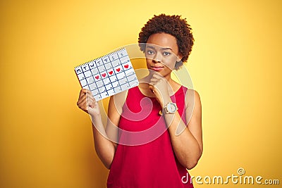 Young african american woman holding menstruation calendar over isolated yellow background serious face thinking about question, Stock Photo