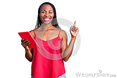 Young african american woman holding touchpad surprised with an idea or question pointing finger with happy face, number one Stock Photo