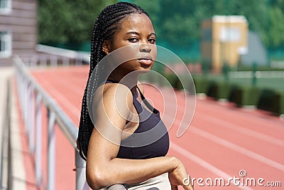 Young African American woman leans on metal fencing of sports ground of big resisential complex Stock Photo