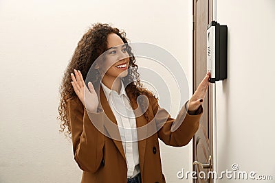 Young African-American woman ringing intercom while waving to camera in entryway Stock Photo