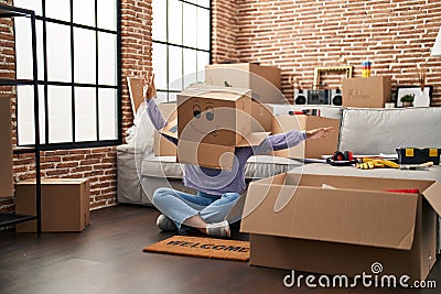 Young african american woman sitting on the floor with funny cardboard box on head at new home Stock Photo