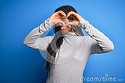 Young african american woman standing wearing casual turtleneck over blue isolated background Doing heart shape with hand and Stock Photo