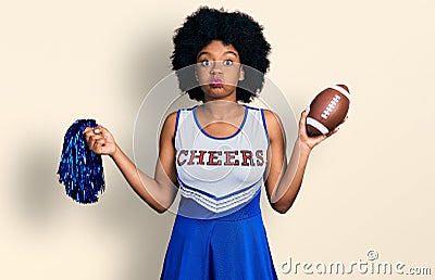Young african american woman wearing cheerleader uniform holding pompom and football ball puffing cheeks with funny face Stock Photo